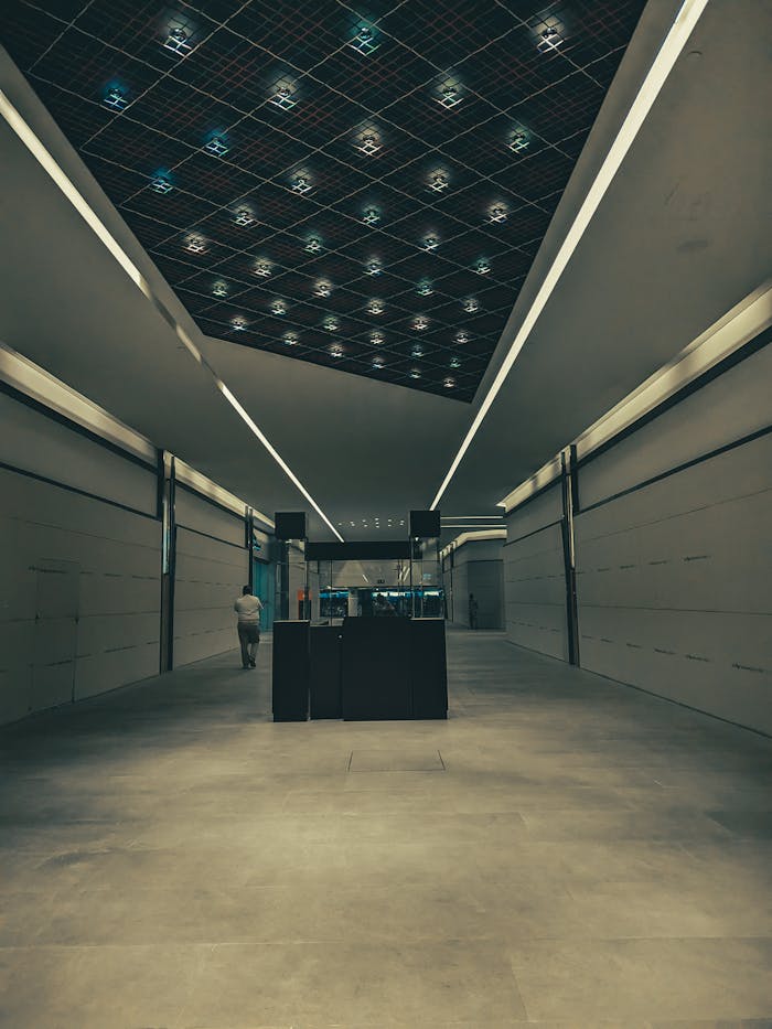 A lone person walking in a modern subway corridor featuring sleek architectural lines and a illuminated ceiling.